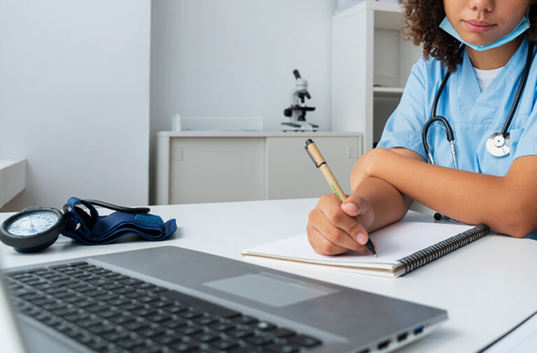 Nurse writing in notebook looking at laptop